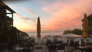 En udendørs terrasse med borde, stole, parasoller og udsigt til solnedgangen.