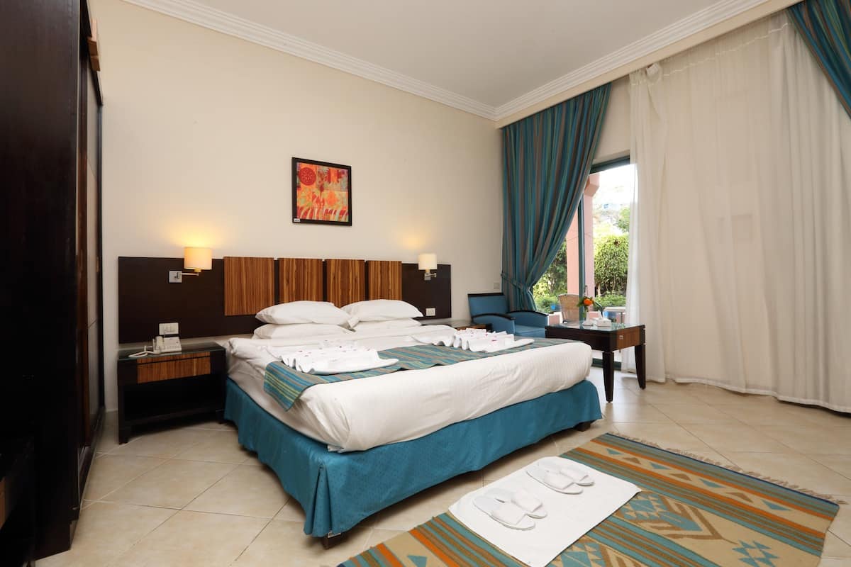 A hotel room with a large bed, a nightstand, a desk, a chair, and a window with curtains.