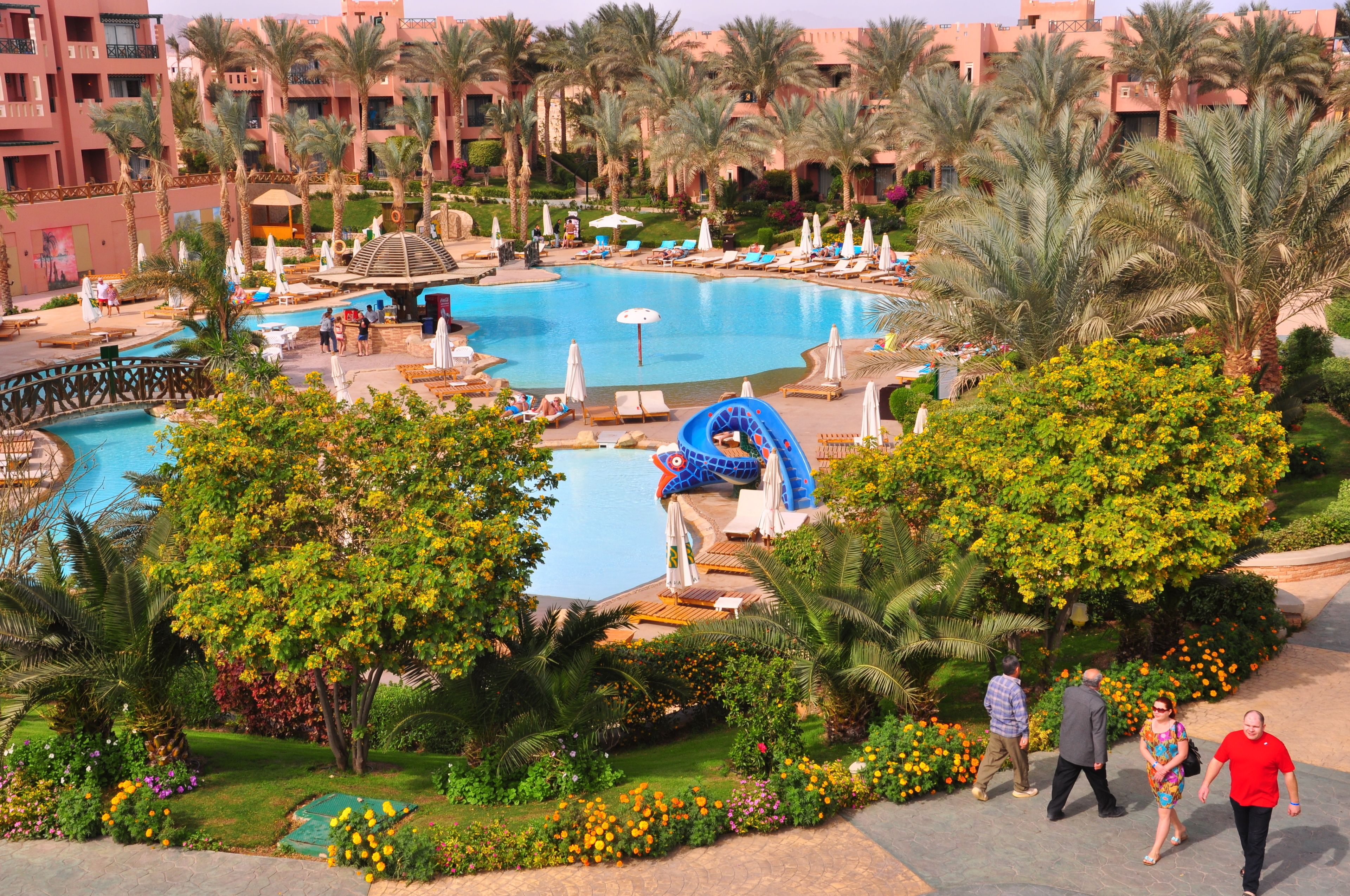 Ein Poolbereich eines Resorts mit Palmen, Liegestühlen und einer Wasserrutsche.