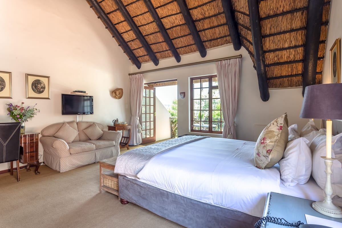 A bedroom with a large bed, a TV, a sofa, and a desk with a lamp.