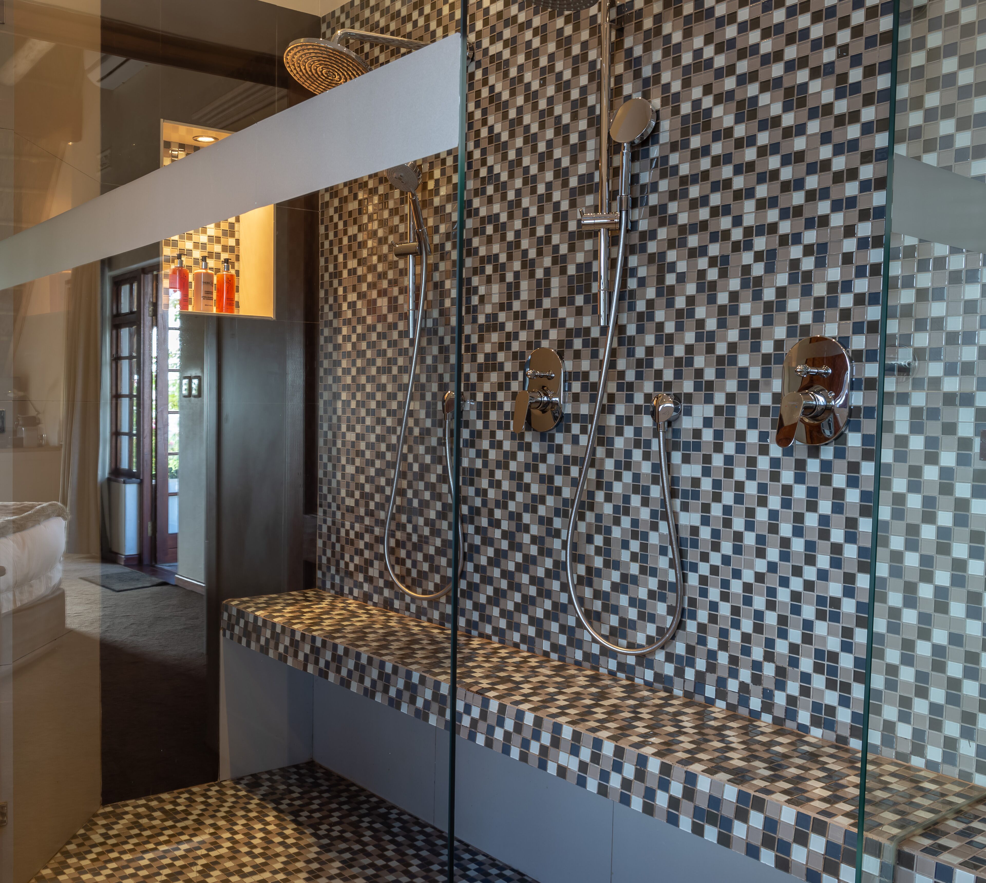 Un baño moderno con pared de baldosas a cuadros, cabina de ducha de vidrio y un banco con artículos de aseo.