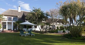 A house with a thatched roof, a covered outdoor seating area with chairs, and a well-maintained lawn. - Wedgeview Country House & Spa (Stellenbosch)