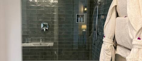A modern bathroom with dark tiled walls, a patterned floor, a glass shower enclosure, and a towel rack with a robe.