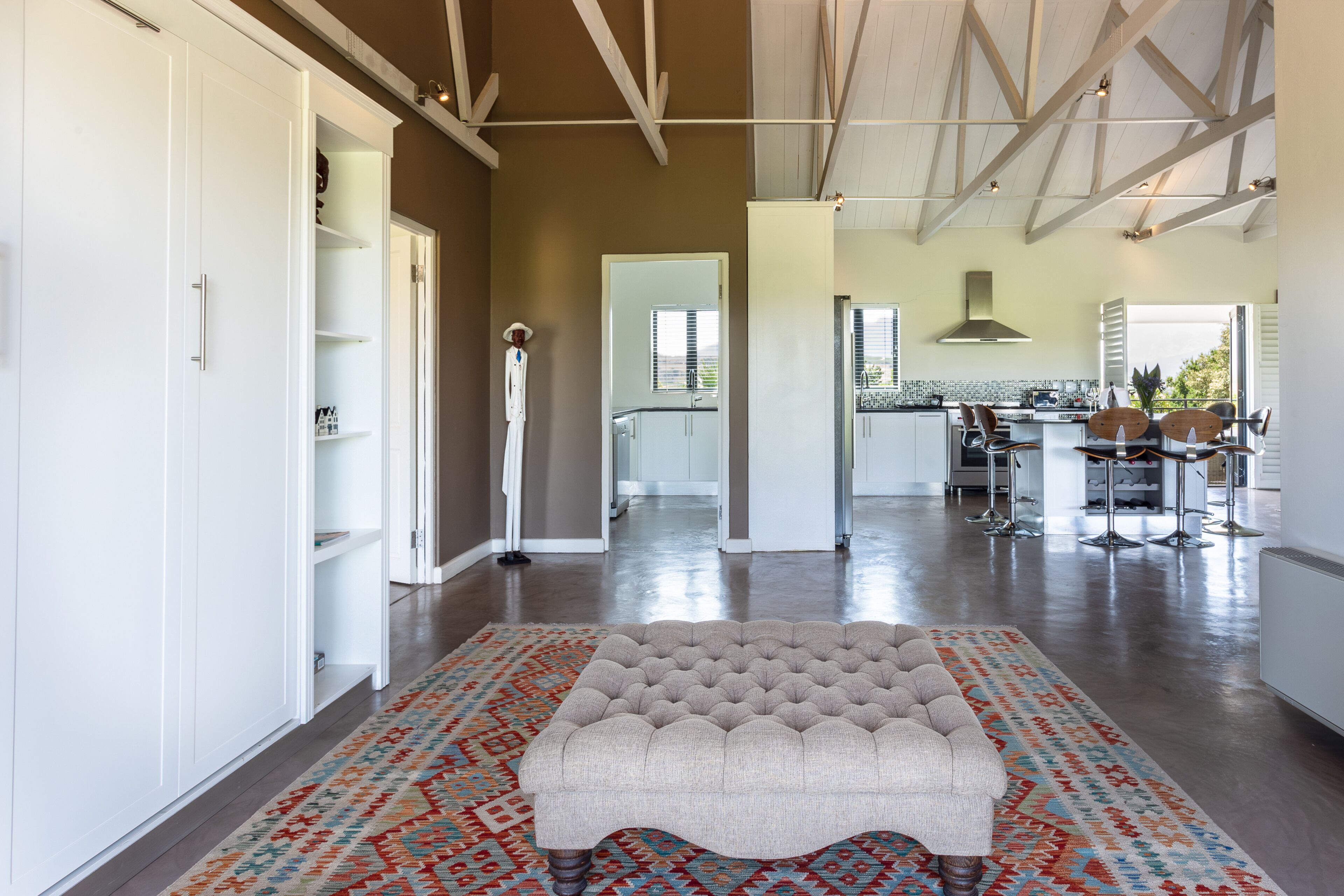 A spacious living area with a tufted sofa, a patterned rug, and a kitchen in the background.