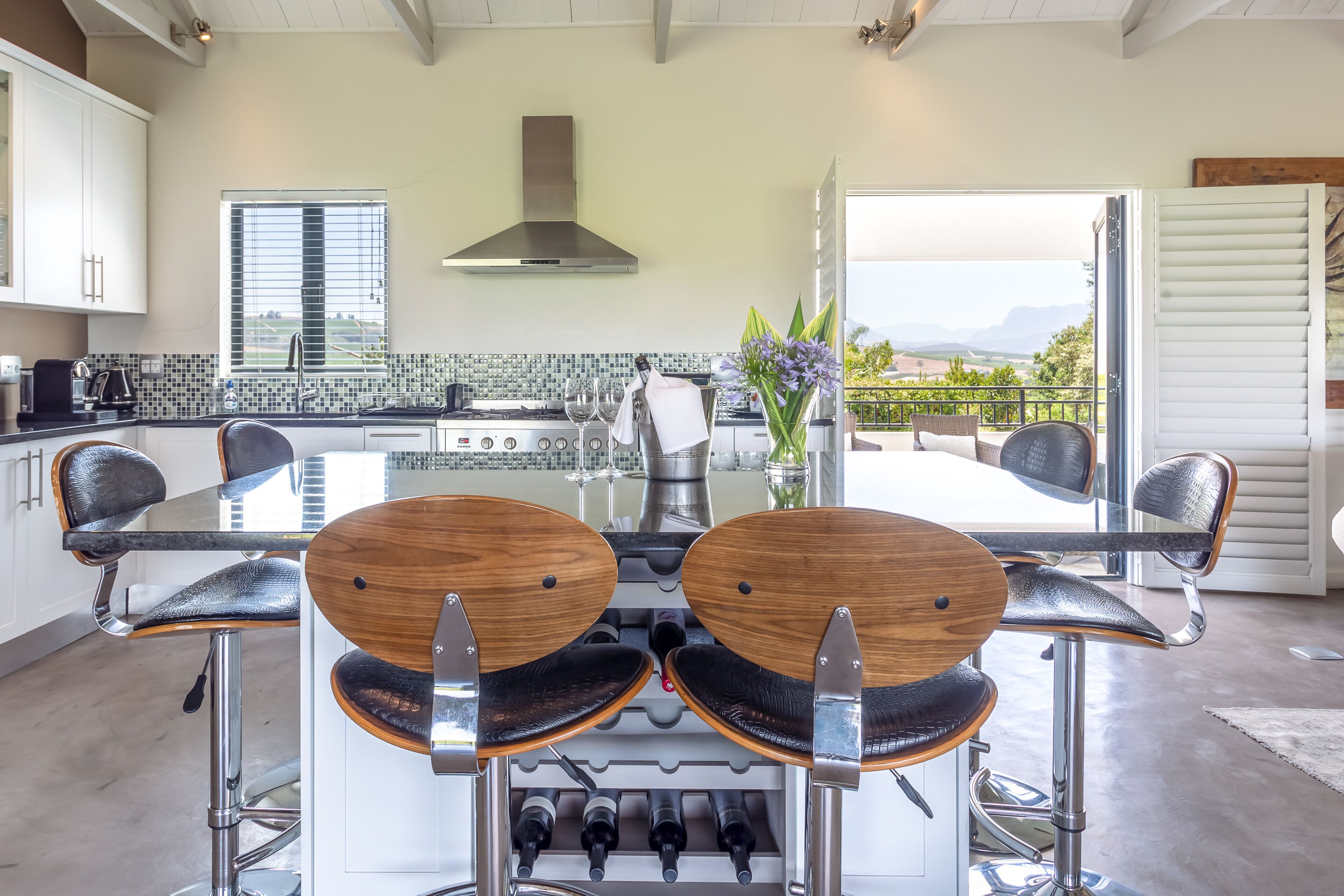 A modern kitchen with a central island, bar stools, and a view to a balcony.