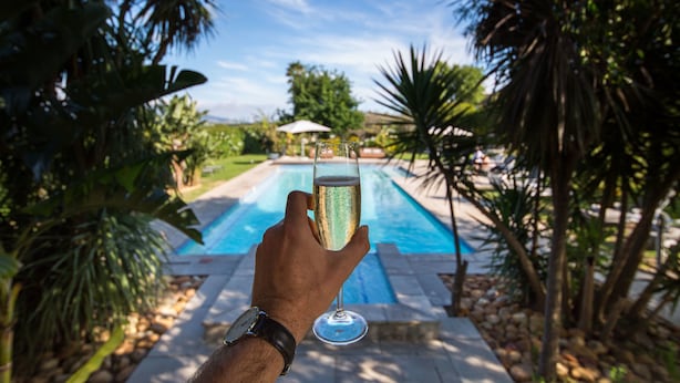 A hand holding a glass of champagne with a pool in the background. - Wedgeview Country House & Spa (Stellenbosch)