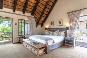 A bedroom with a large bed, a nightstand, a bedside table, a bench, and a window with curtains. - Wedgeview Country House & Spa (Stellenbosch)