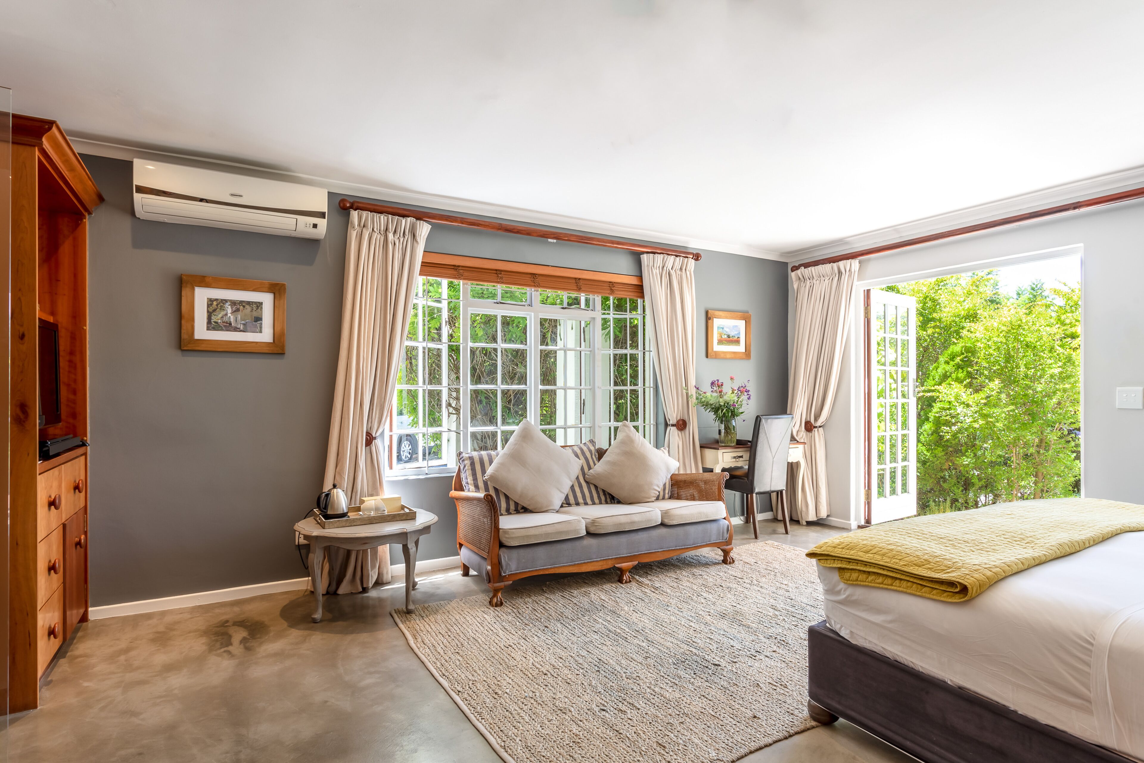A bedroom with a large bed, a sofa, a window with curtains, a small table, and a wardrobe.