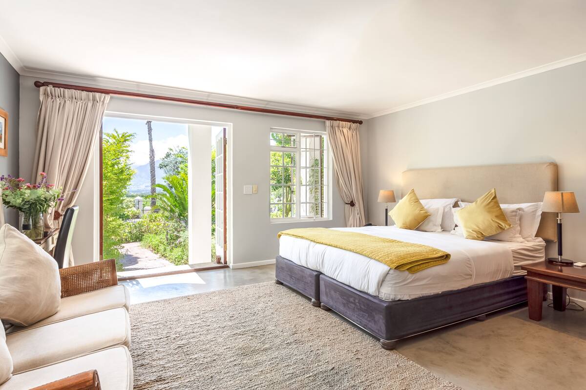 A spacious bedroom with a large bed, a sofa, and a view of greenery through the window.
