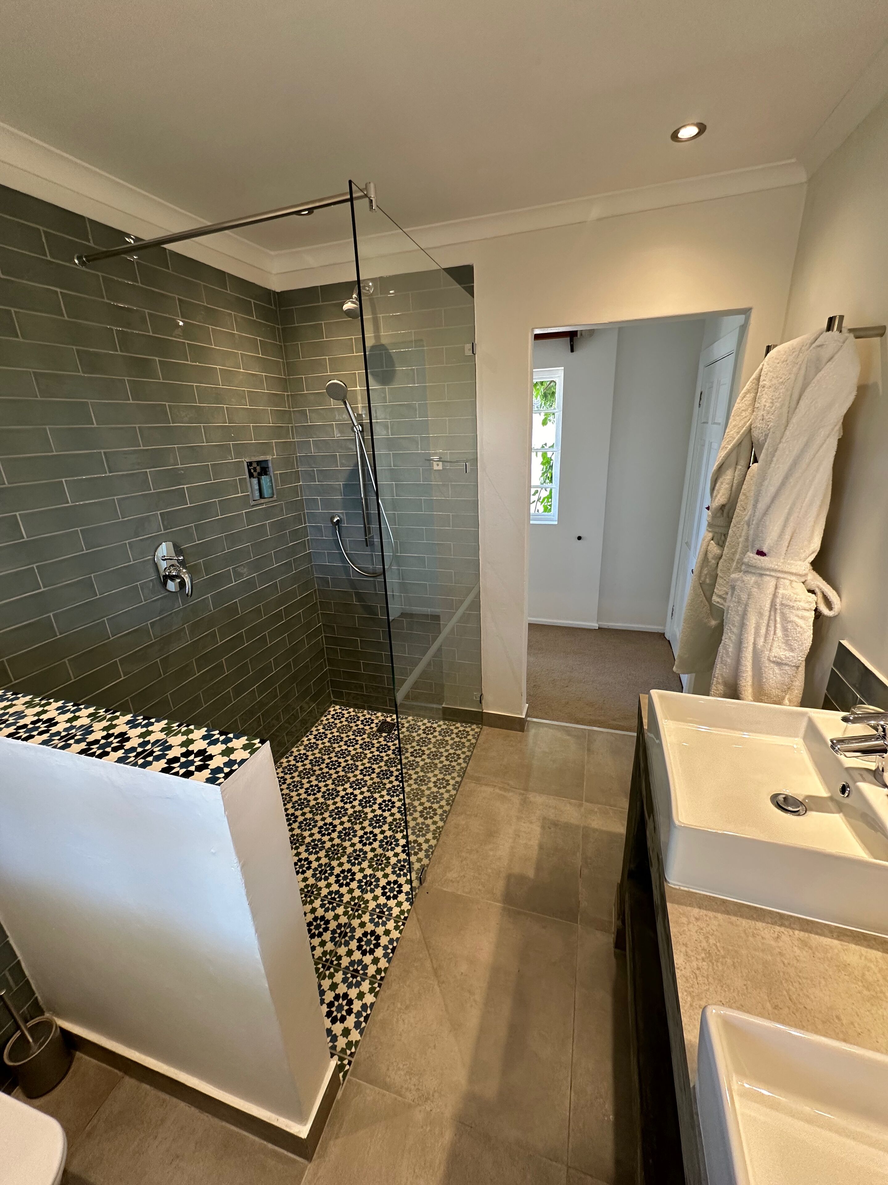A modern bathroom with a glass-enclosed shower, a white bathtub, and two sinks.