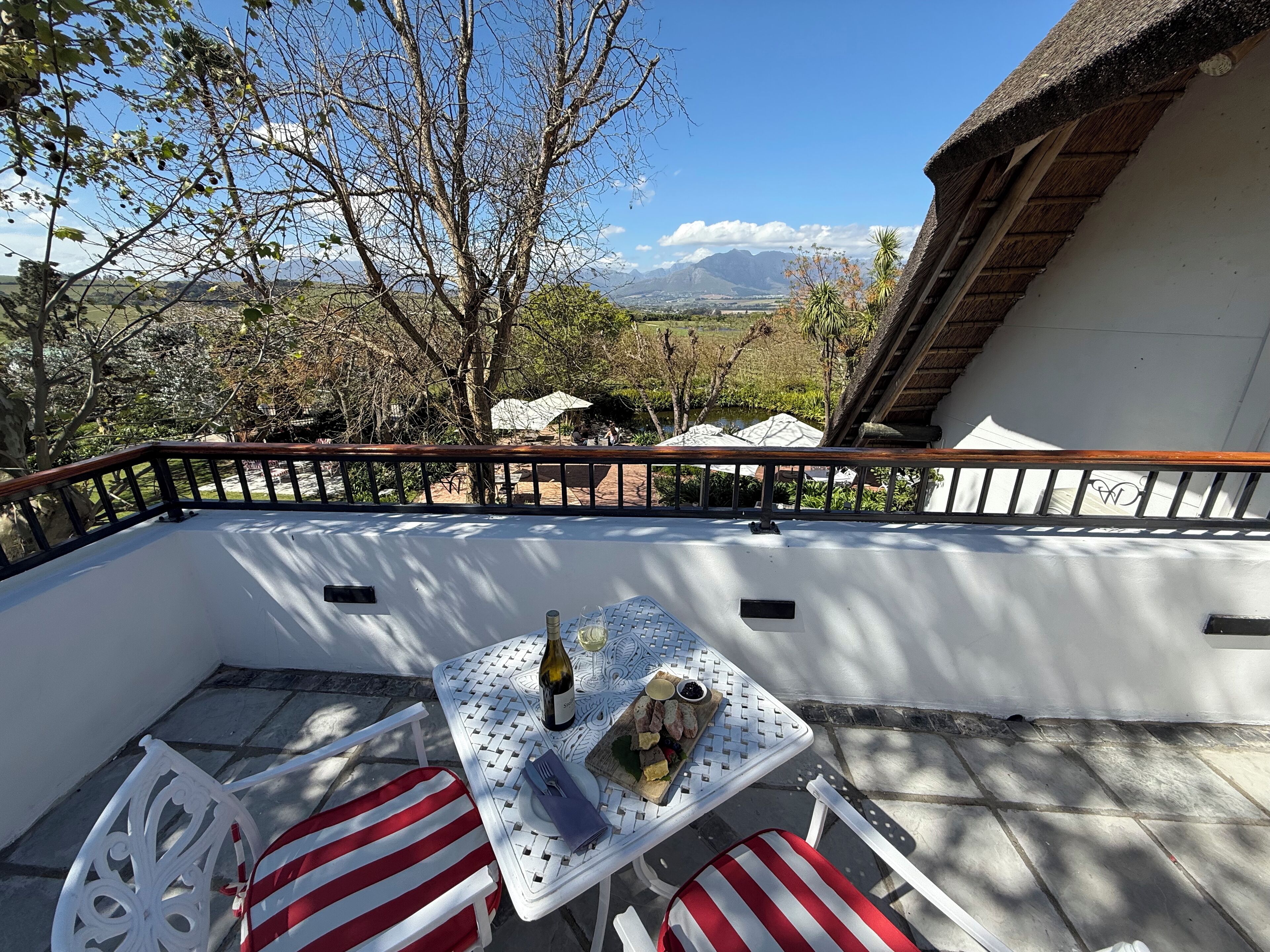 A balcony with a table set for two, a bottle of wine, and a plate of food.