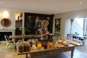A breakfast buffet with various food and drink options, a fireplace, and a wine rack in the background. - Wedgeview Country House & Spa (Stellenbosch)