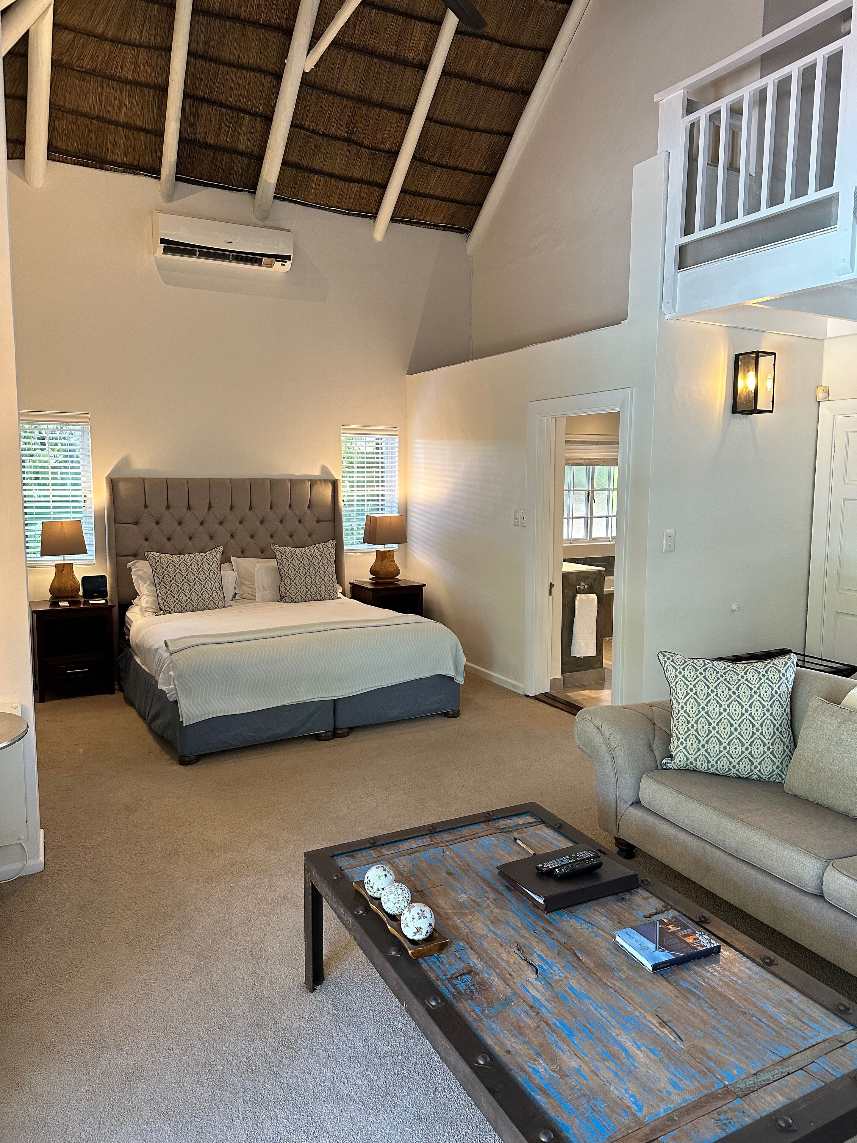 A spacious bedroom with a large bed, two bedside tables with lamps, a wooden coffee table with decorative items, and a balcony with a railing.