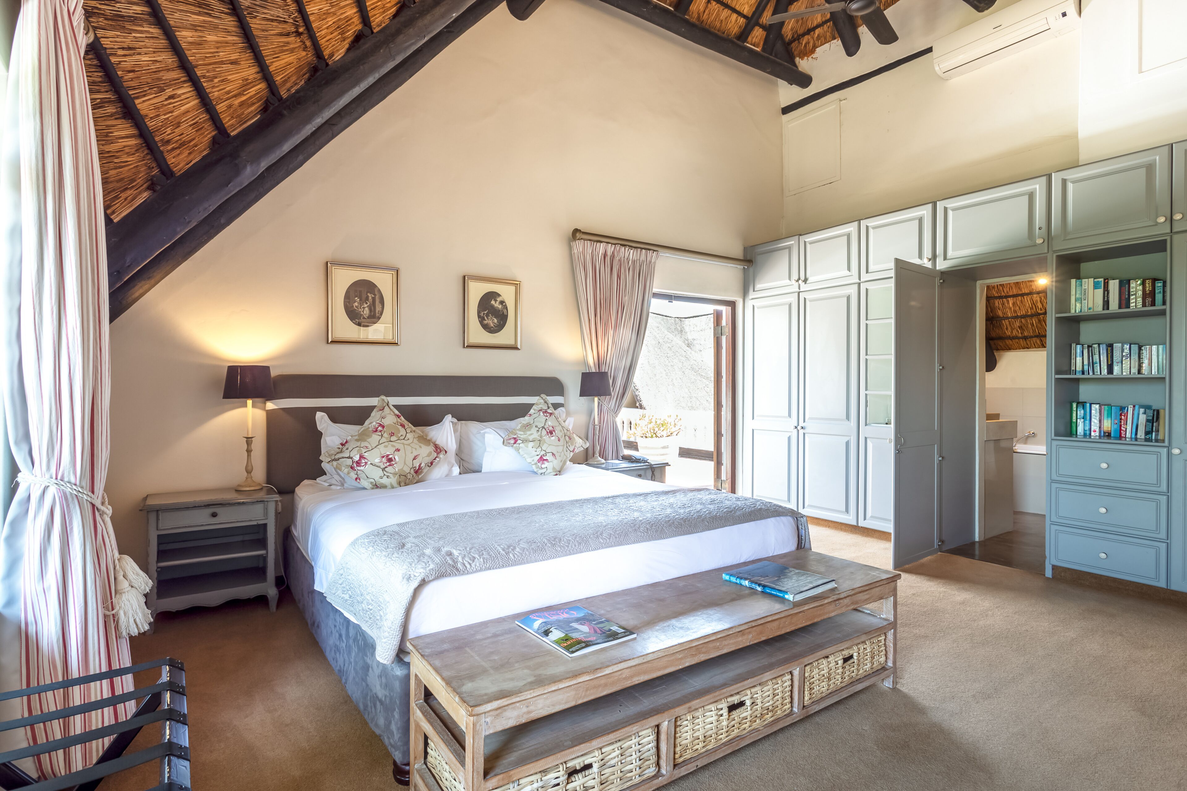 A bedroom with a large bed, bedside tables, a wooden bench, a wardrobe, and a bookshelf.