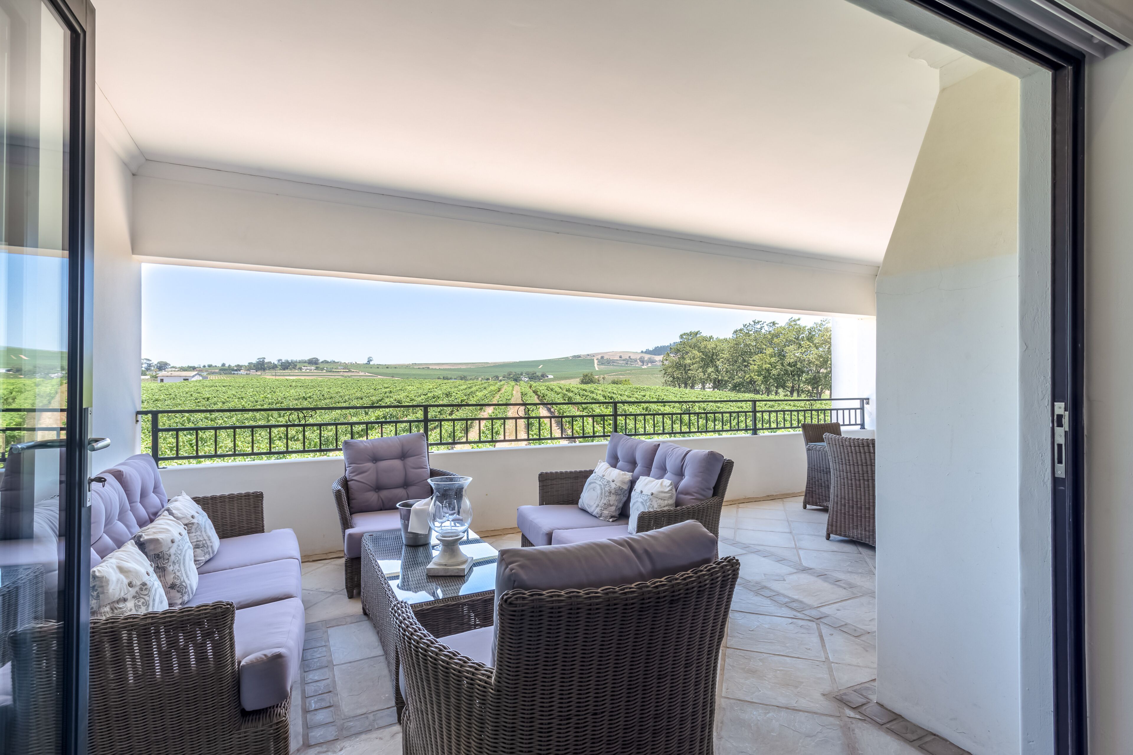 A balcony with wicker furniture, a glass table, and a view of a green landscape.