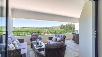 A balcony with wicker furniture, a glass table, and a view of a green landscape.