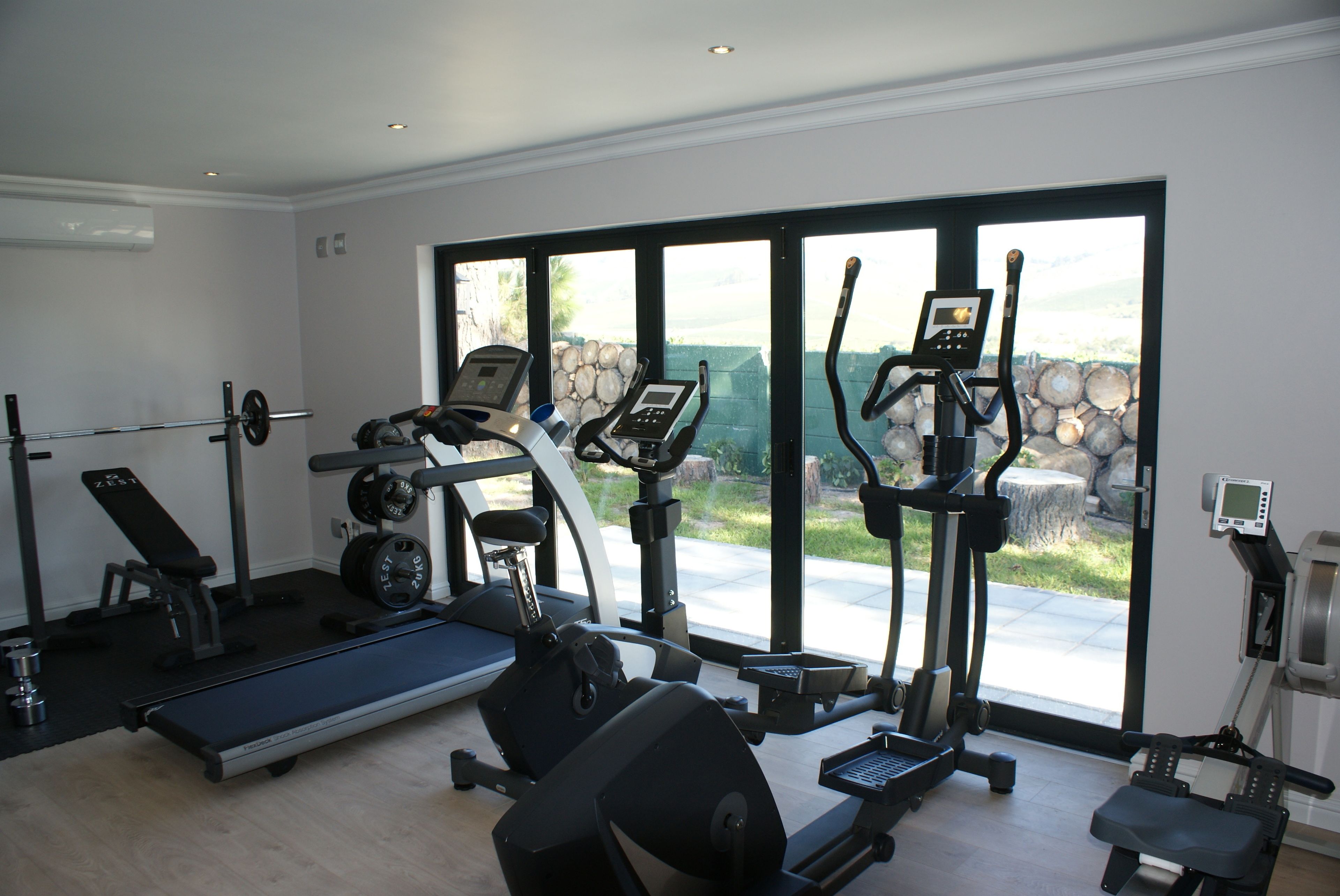 Gimnasio en casa con cinta de correr, elíptica, bicicleta estática y banco de pesas.