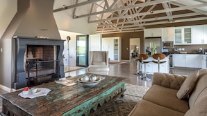 A spacious living area with a fireplace, a rustic coffee table, and a modern kitchen in the background. - Wedgeview Country House & Spa (Stellenbosch)