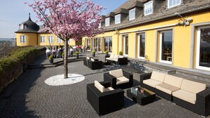 An outdoor seating area with wicker furniture and a tree with pink blossoms. - Hotel Schloss Montabaur (Montabaur)