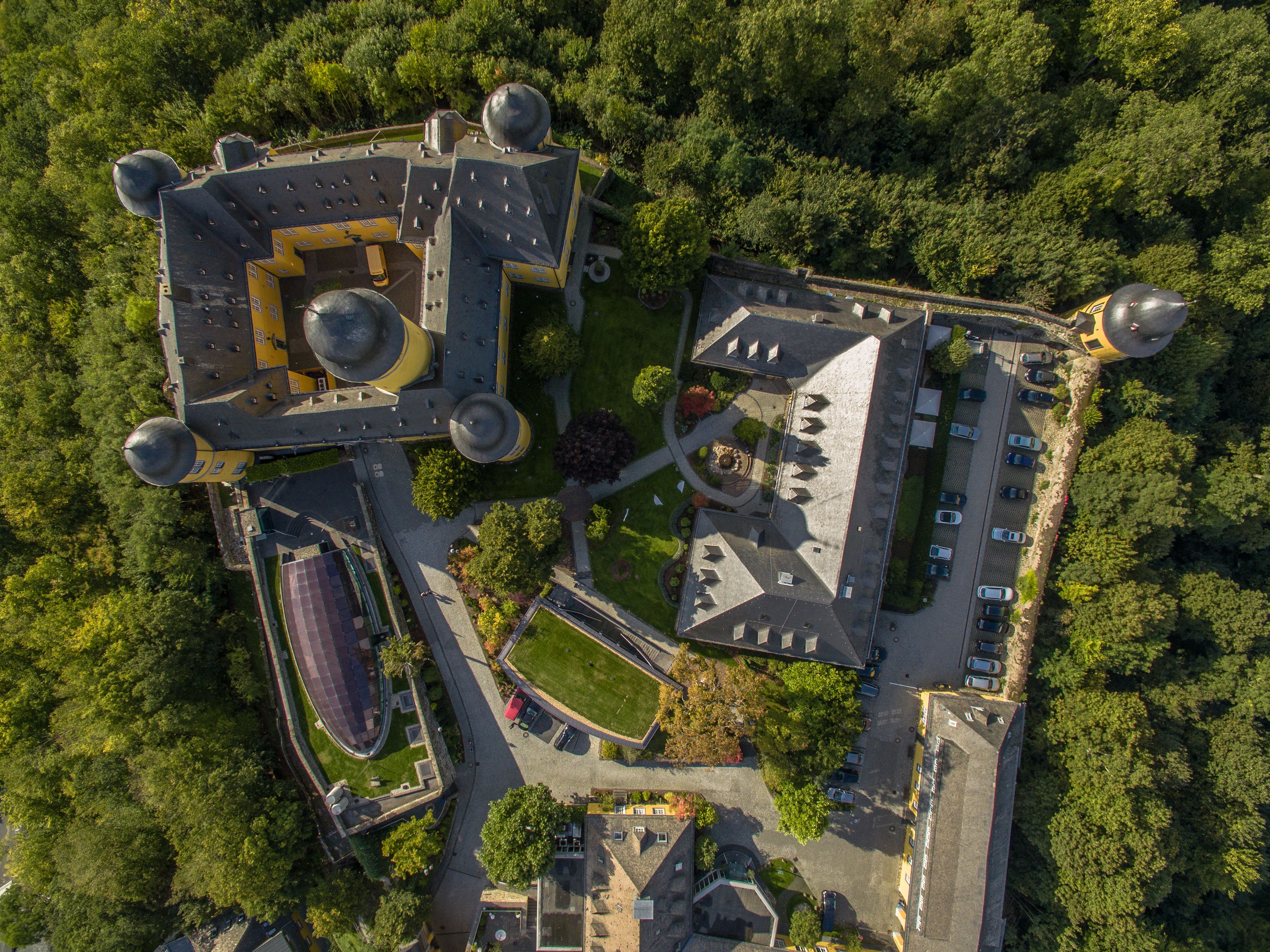 Vista aérea de un complejo con varias construcciones, incluyendo una estructura central grande con una cúpula y varias cúpulas más pequeñas, rodeado de áreas de estacionamiento y zonas verdes.