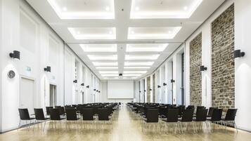 Sala de conferências com fileiras de cadeiras pretas, um quadro branco e uma parede de pedra decorativa.