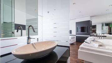 A modern bathroom with a large vessel sink, a mirror, and a wooden floor.