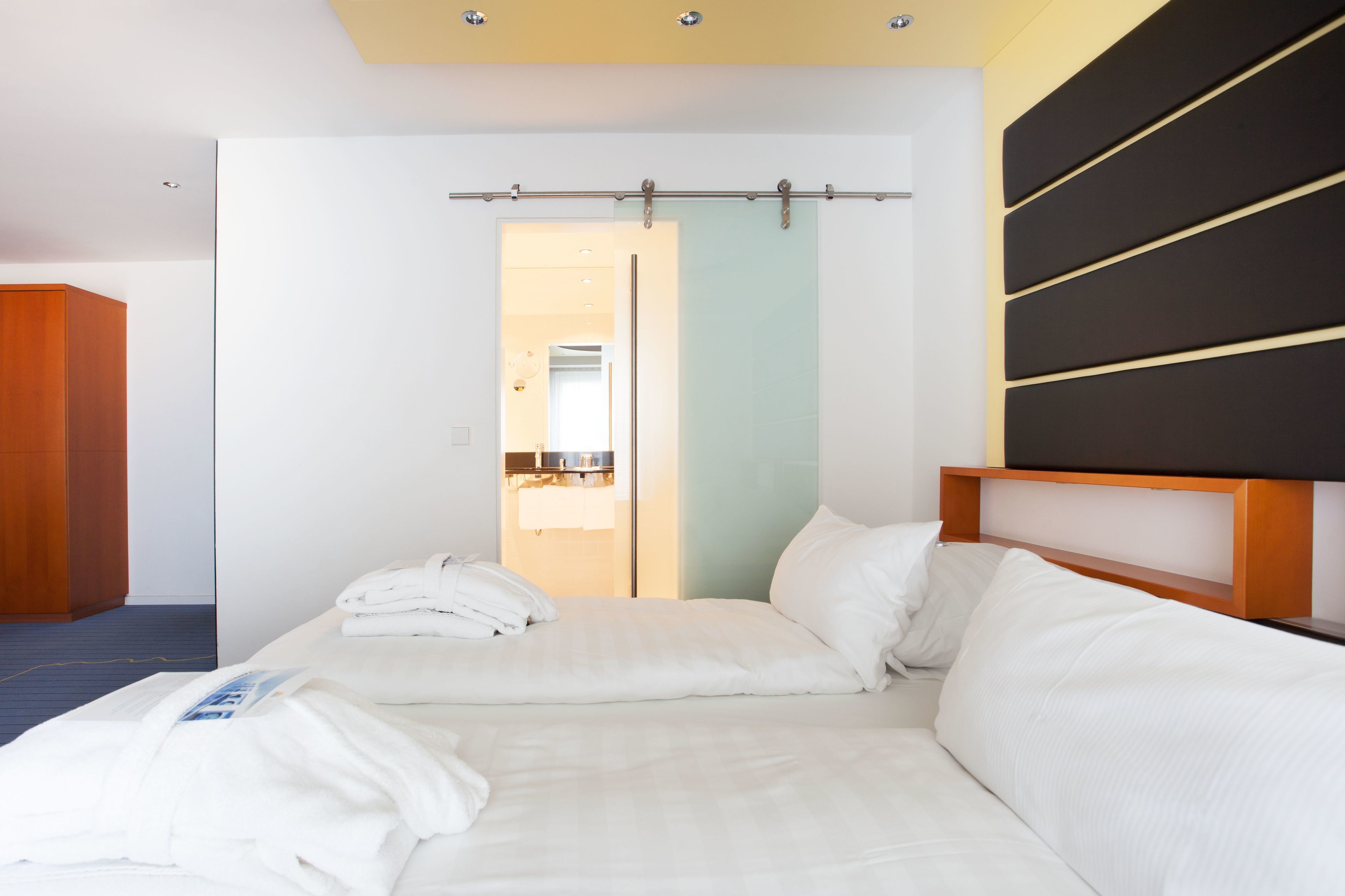A hotel room with a bed, a wooden wardrobe, and a bathroom visible through an open door.