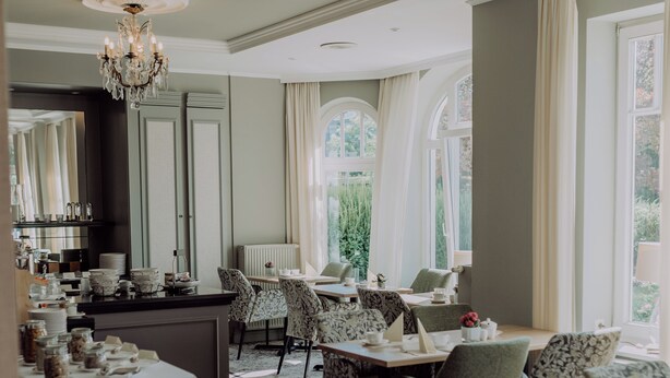 A dining area with tables set for service, a chandelier, and large windows with curtains. - Hotel Jungclaus (Wentorf bei Hamburg)