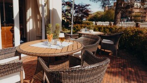 An outdoor patio with wicker furniture, a table with a glass of beer, and an umbrella. - Hotel Jungclaus (Wentorf bei Hamburg)
