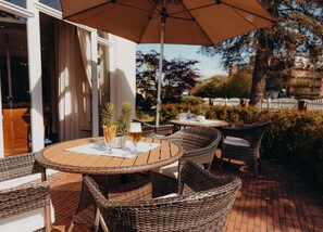 An outdoor patio with wicker furniture, a table with a glass of beer, and an umbrella. - Hotel Jungclaus (Wentorf bei Hamburg)
