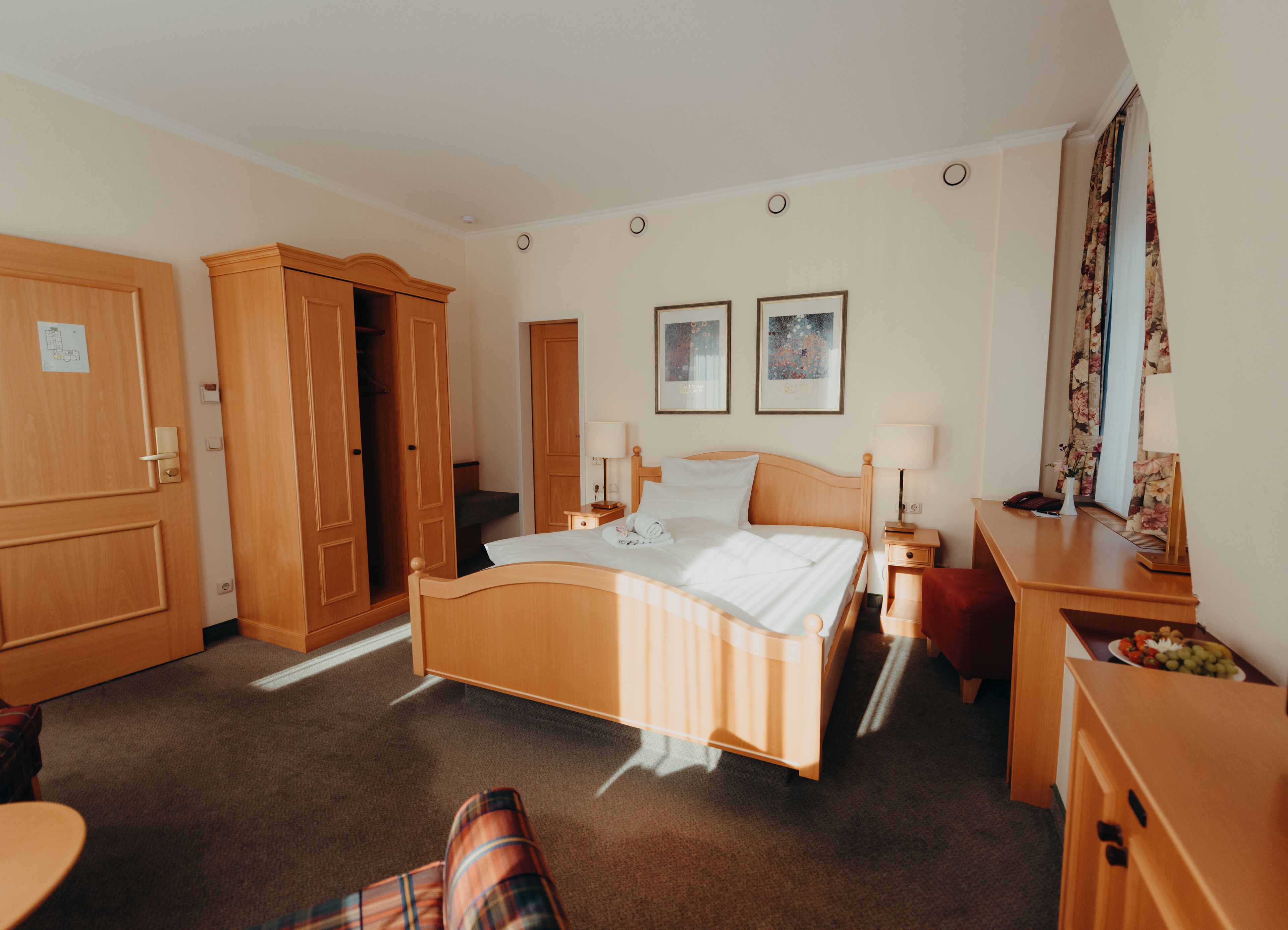 Una habitación de hotel con cama, armario de madera, mesitas de noche y un escritorio con lámpara.