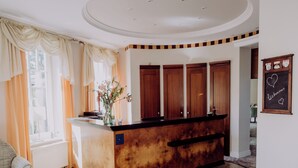A reception area with a wooden reception desk, a large window with curtains, a patterned carpet, and a wall-mounted sign with a heart symbol.
