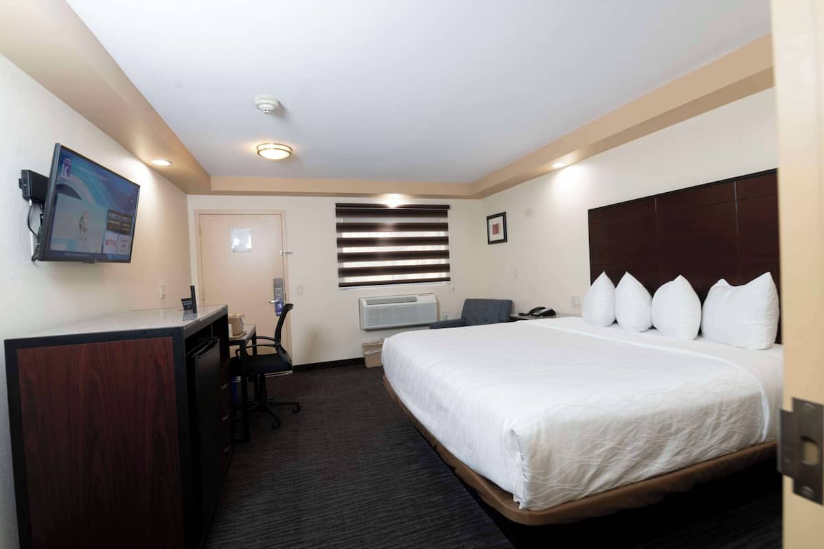 A hotel room with a bed, desk, chair, and a television on the wall.