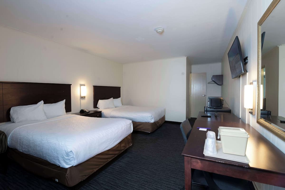 A hotel room with two beds, a desk, a television, and a mirror.