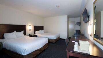 A hotel room with two beds, a desk, a television, and a mirror.