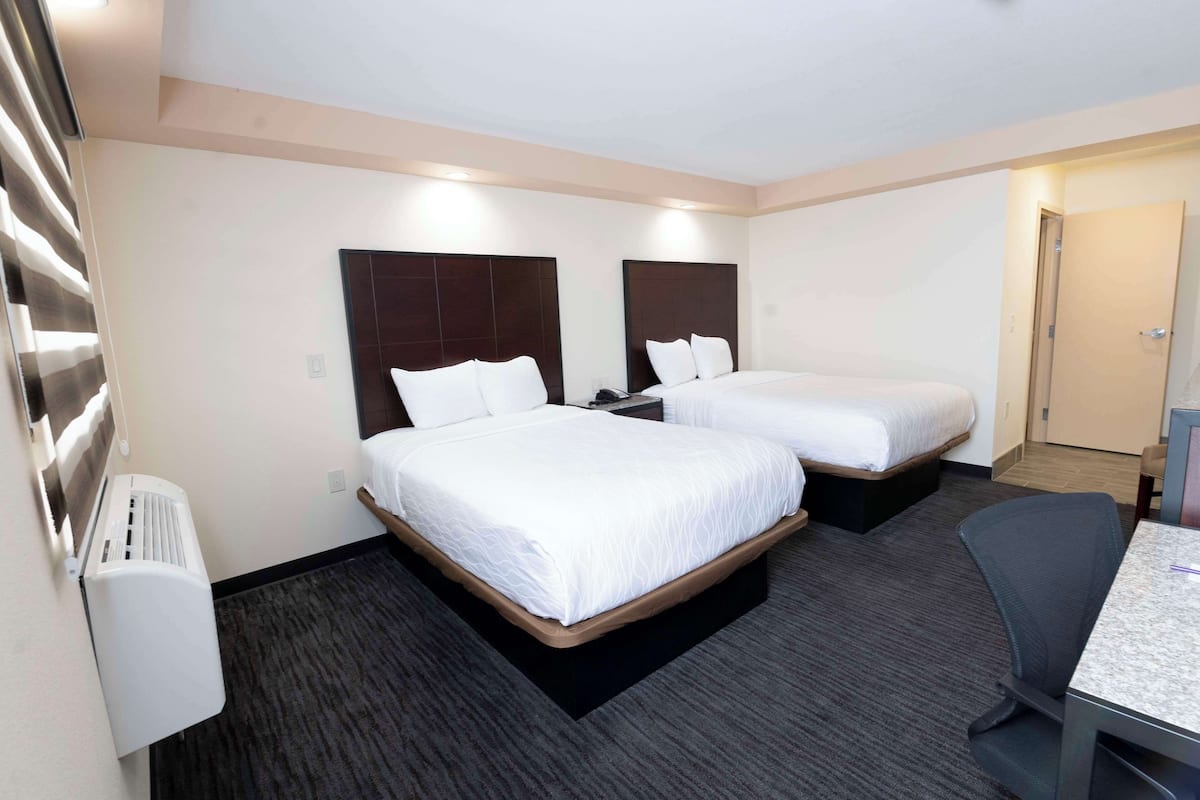 A hotel room with two beds, a desk, and a chair.