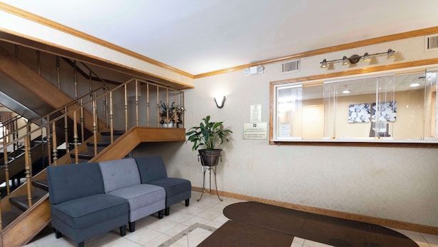A reception area with a staircase, a sofa, a potted plant, and a mirror. - Knights Inn South Amboy (South Amboy)
