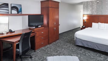 Habitación de hotel con escritorio de madera, televisor, cama y armario.