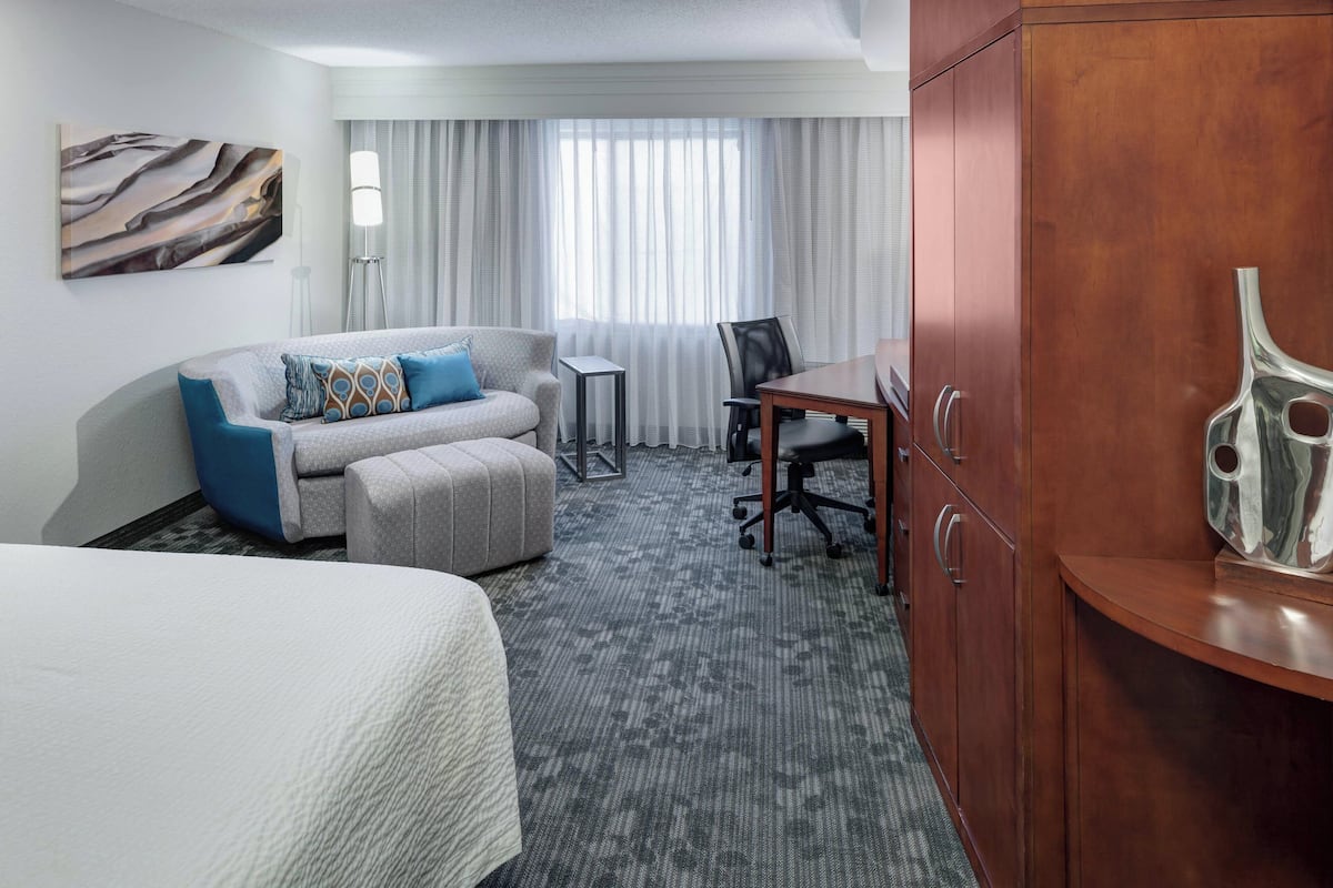 Ein Hotelzimmer mit Bett, Sofa, Fußschemel, Schreibtisch und Schrank.