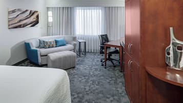 Una habitación de hotel con una cama, un sofá con reposapiés, un escritorio y un armario.