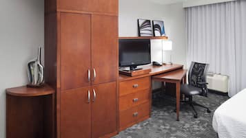A hotel room with a wooden desk, a television, a chair, and a bed.