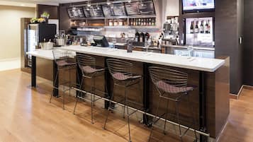 Un área de bar moderna con una barra larga, taburetes, una pantalla de televisión y un enfriador de vino.