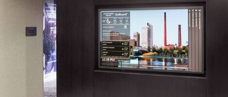 A digital display in a hotel lobby with a cityscape view, including tall buildings and a body of water.