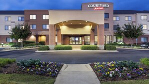 Un hôtel Courtyard Marriott avec une façade en briques, une entrée centrale et un parterre fleuri coloré à l’avant.