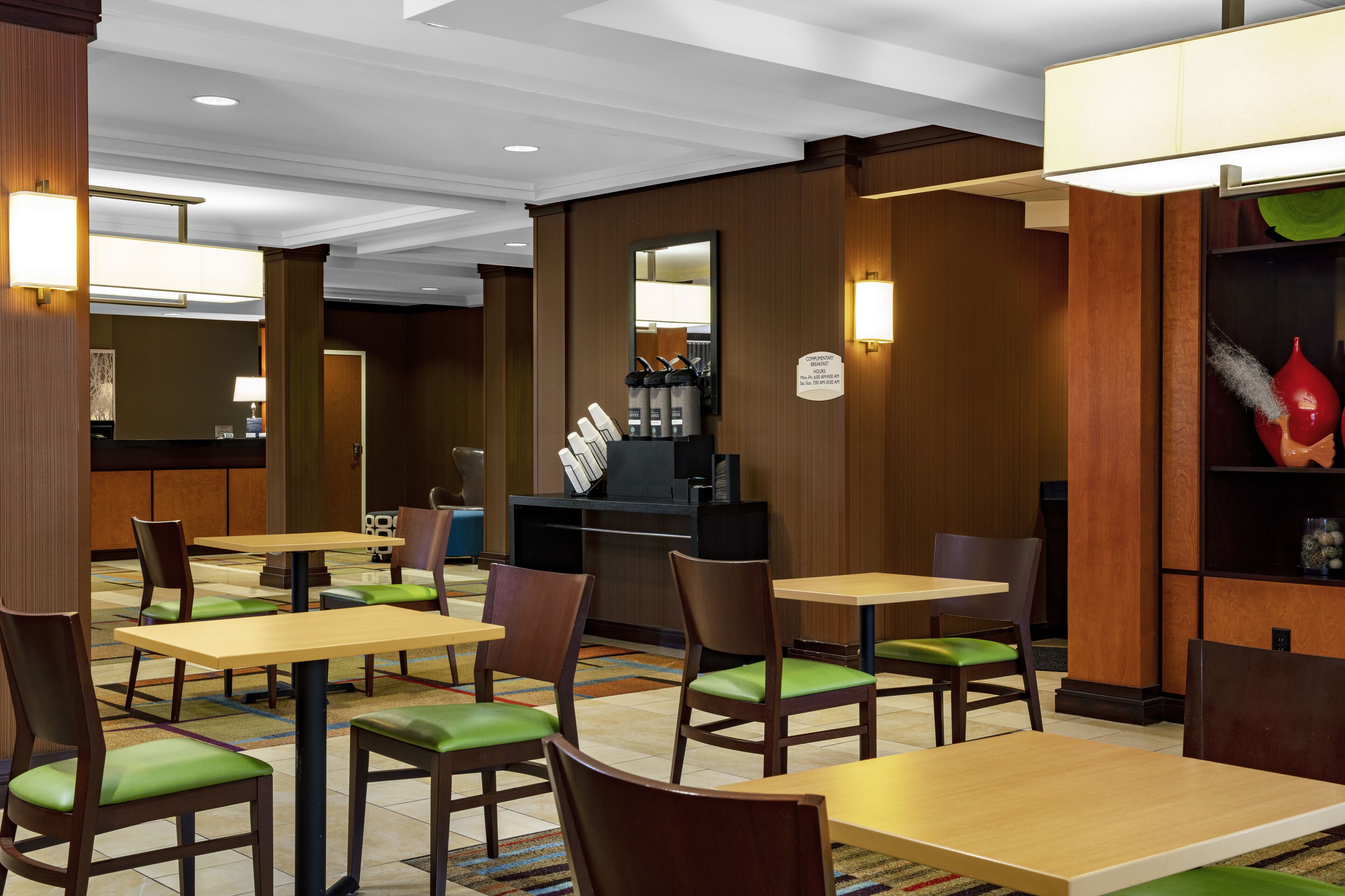 Un vestíbulo de hotel con varias mesas y sillas, una recepción y una máquina de café.