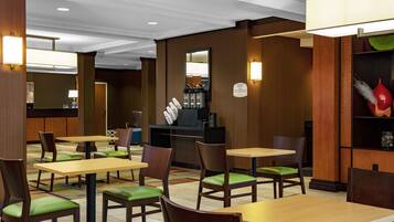 Un vestíbulo de hotel con varias mesas y sillas, una recepción y una máquina de café.