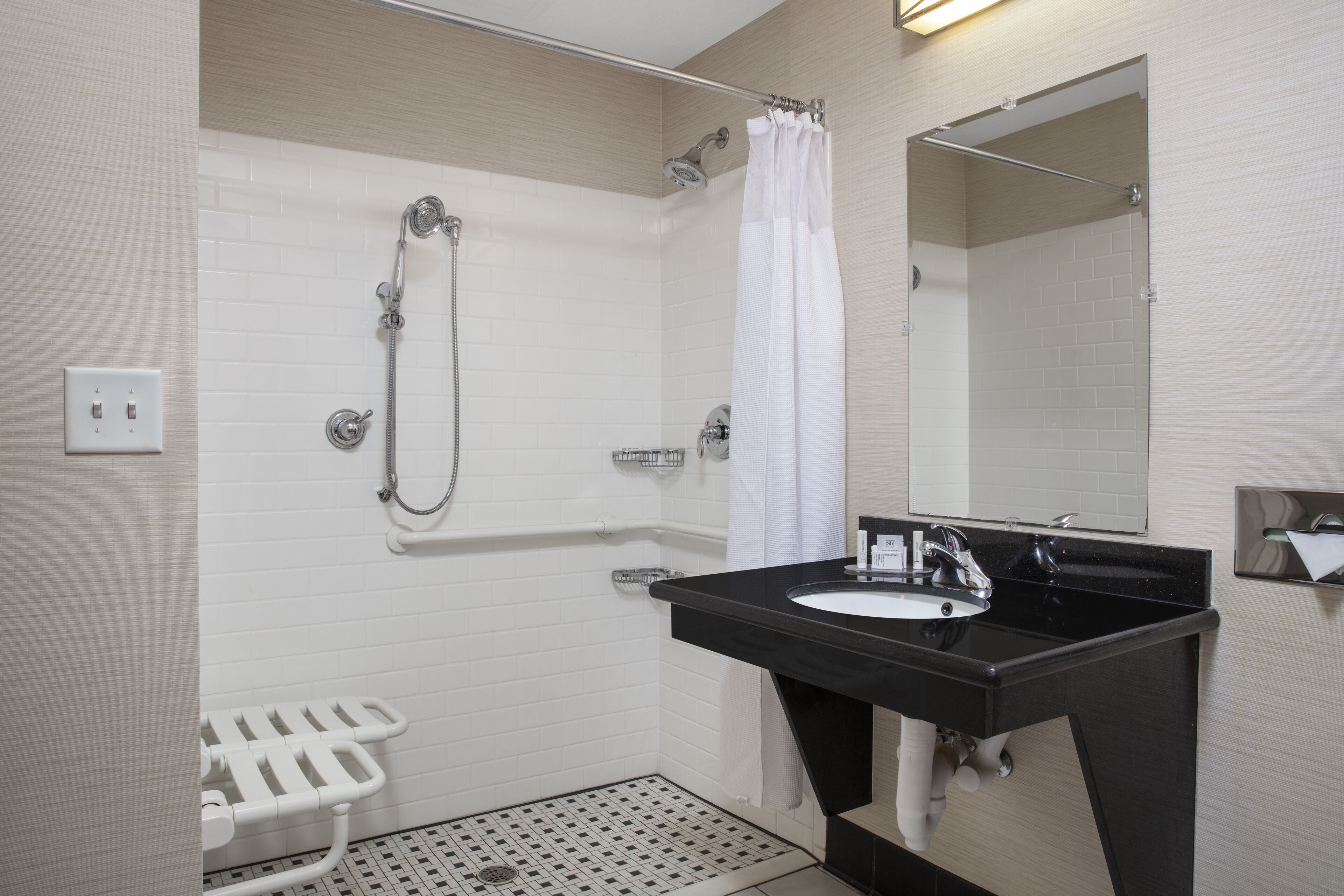 A modern bathroom with a black sink, white shower, and a white toilet with a safety bar.