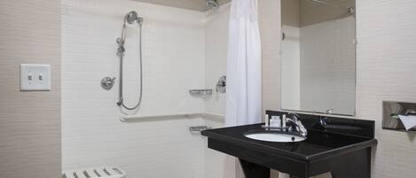 A modern bathroom with a black sink, white shower, and a white toilet with a safety bar.