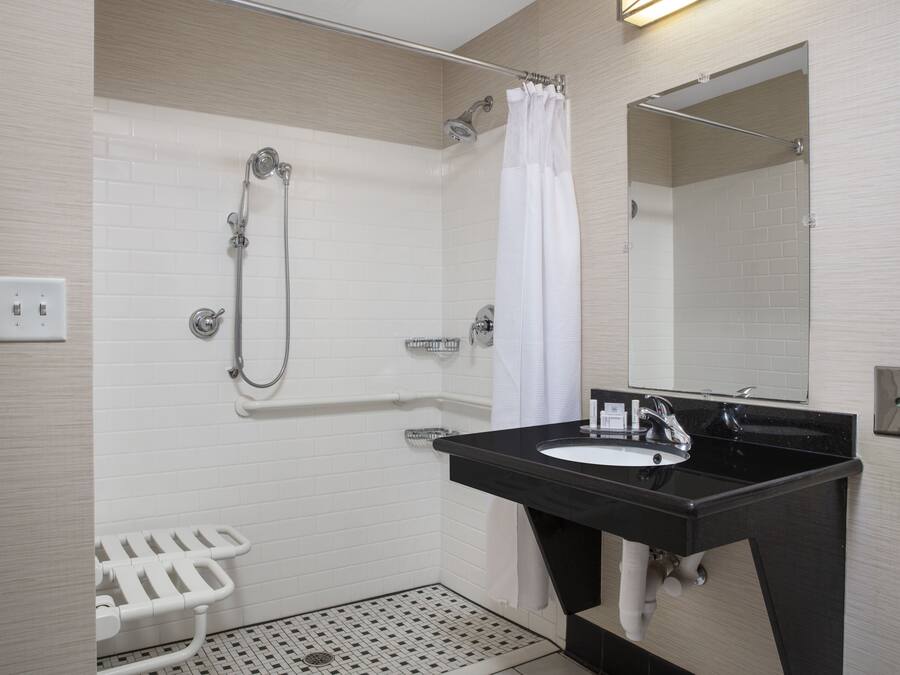A modern bathroom with a black sink, white shower, and a white toilet with a safety bar.