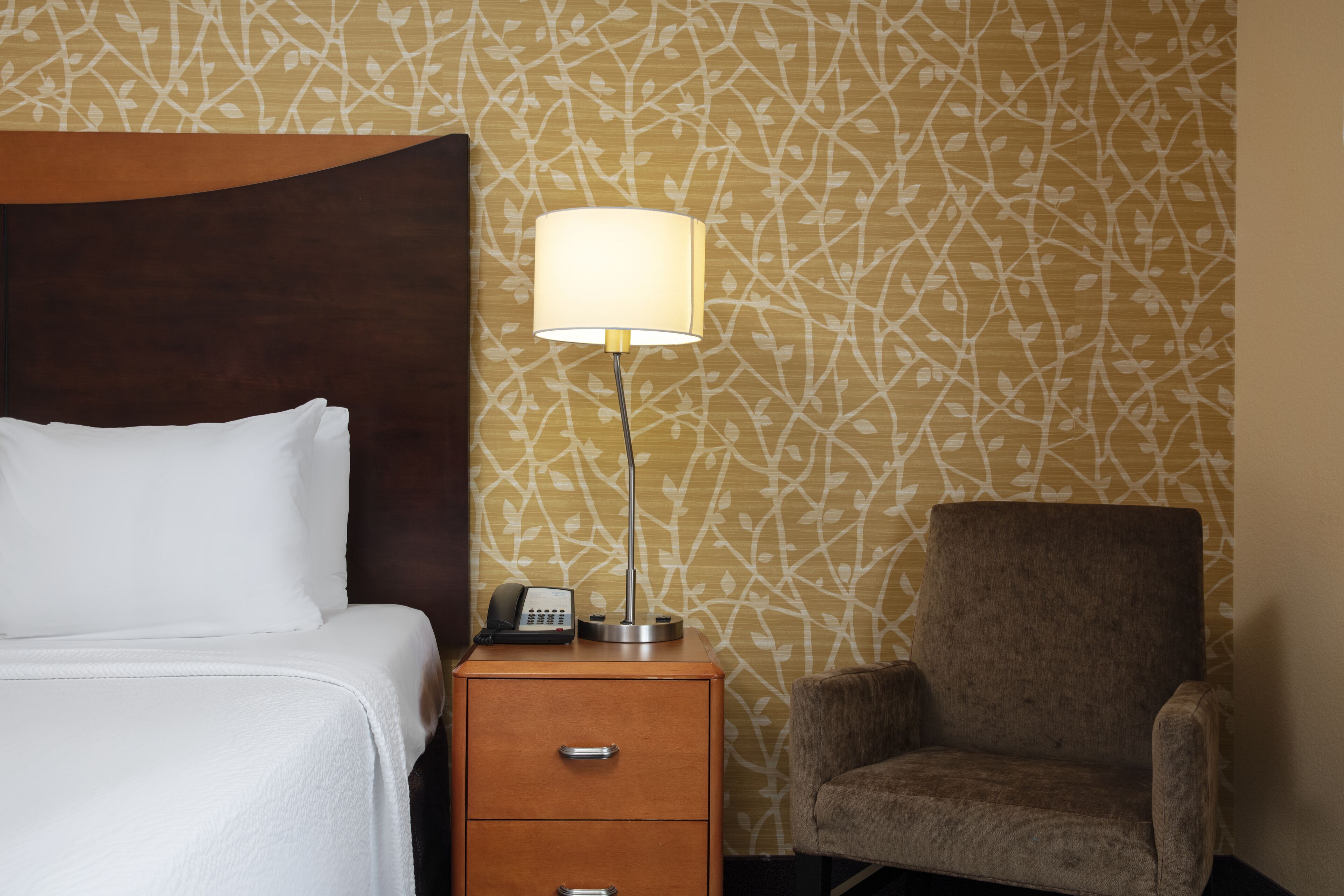 A hotel room with a bed, a nightstand with a lamp, and a chair.